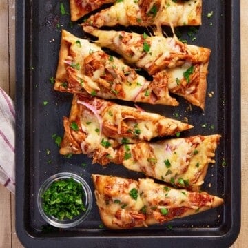 Slices of BBQ Chicken Flatbread on a black sheetpan.