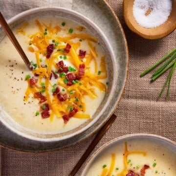 Bowls of baked potato soup topped with bacon, cheese and chives.