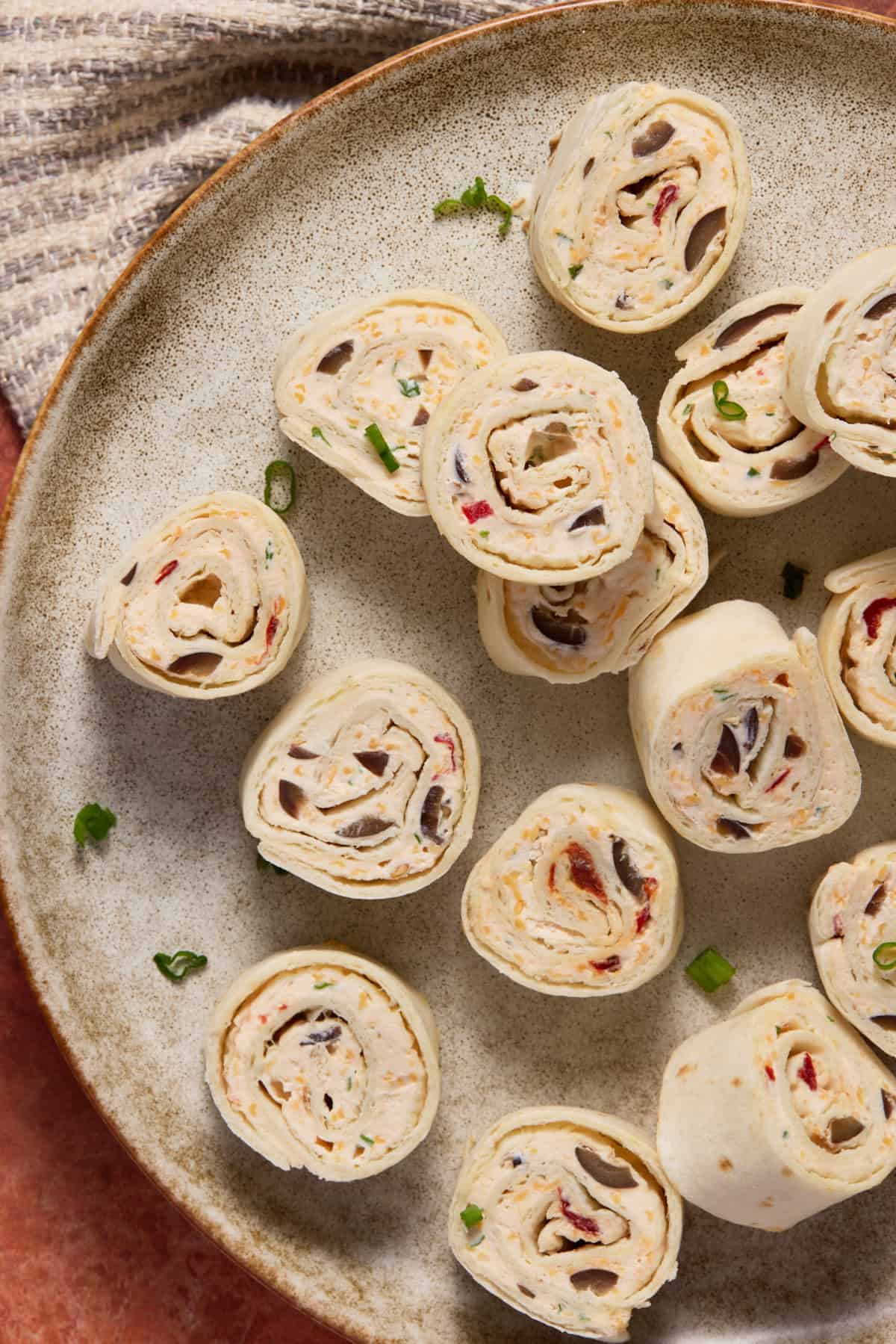 Cream cheese filled tortillas rolled up and sliced on plate.