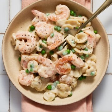 Shrimp,pasta and peas on a plate with a fork and napkin.